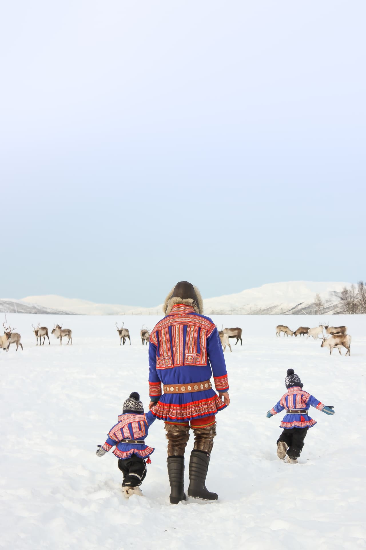 Family in traditional Sámi dress walking out to the reindeer herd